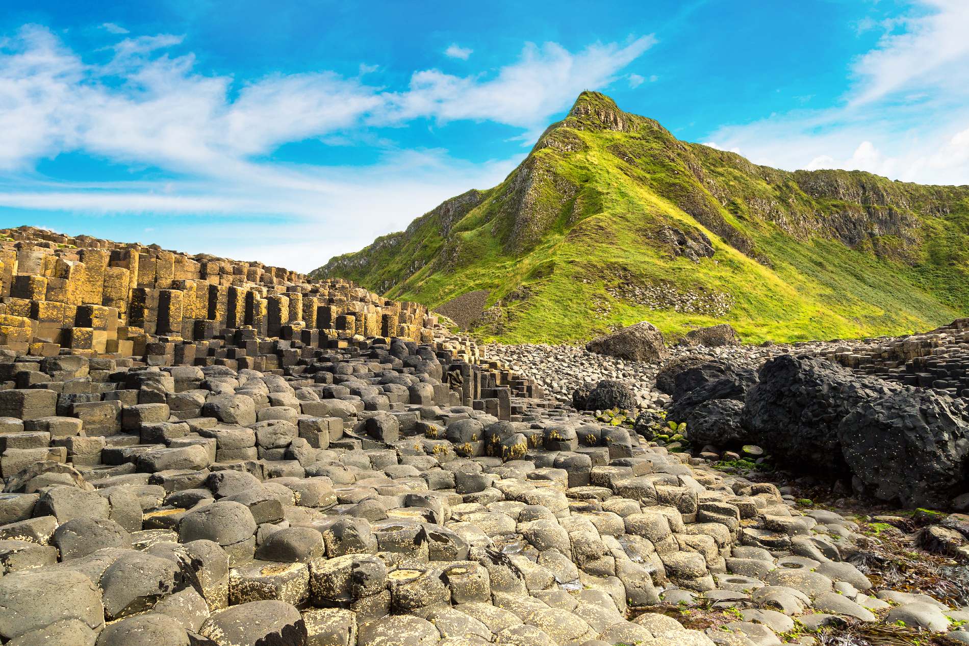 Hexagonal basalt columns rising below a grassy peak on the Giant’s Causeway World Heritage Site trail.
