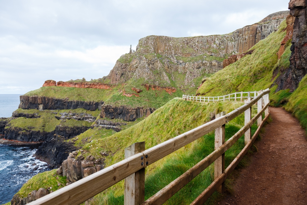 Wooden-railed trail curving past layered cliffs and sea views on a coastal walk near Giant’s Causeway.