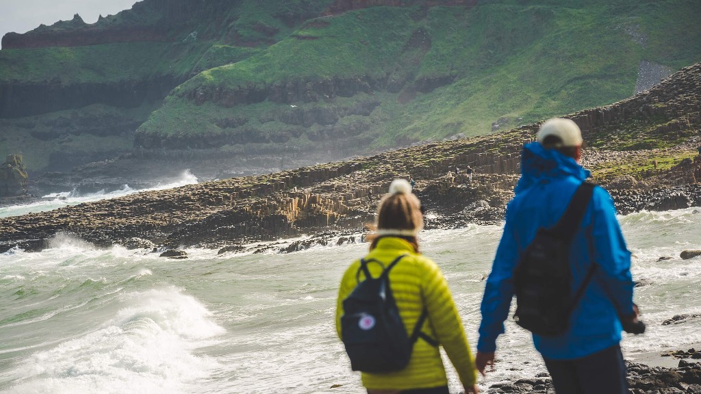 Two walkers in bright jackets on a windswept beach near Giant’s Causeway basalt rocks in County Antrim.
