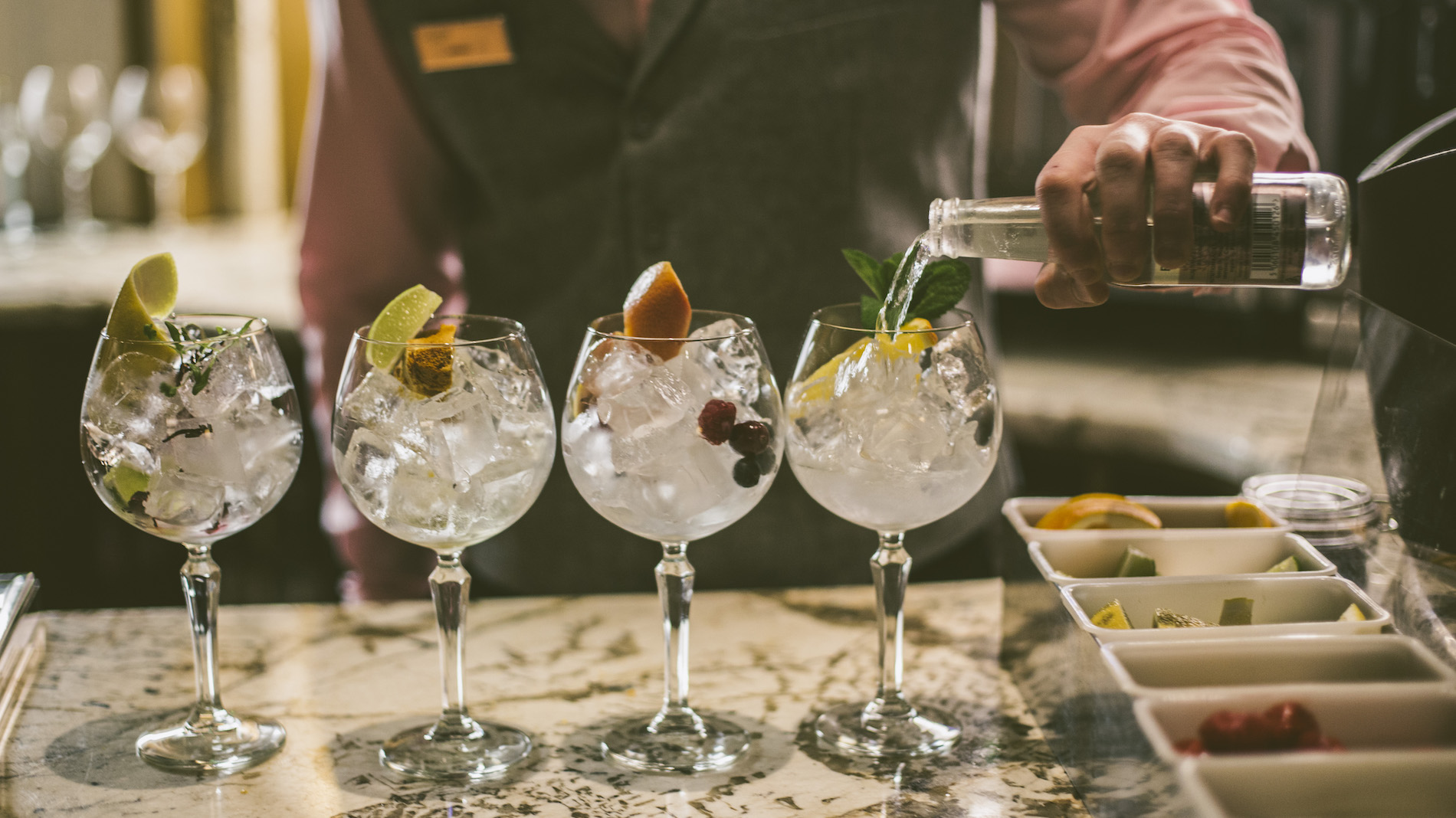 Bartender pouring tonic into gin and tonic glasses with fruit garnishes at Galgorm Resort in County Antrim.