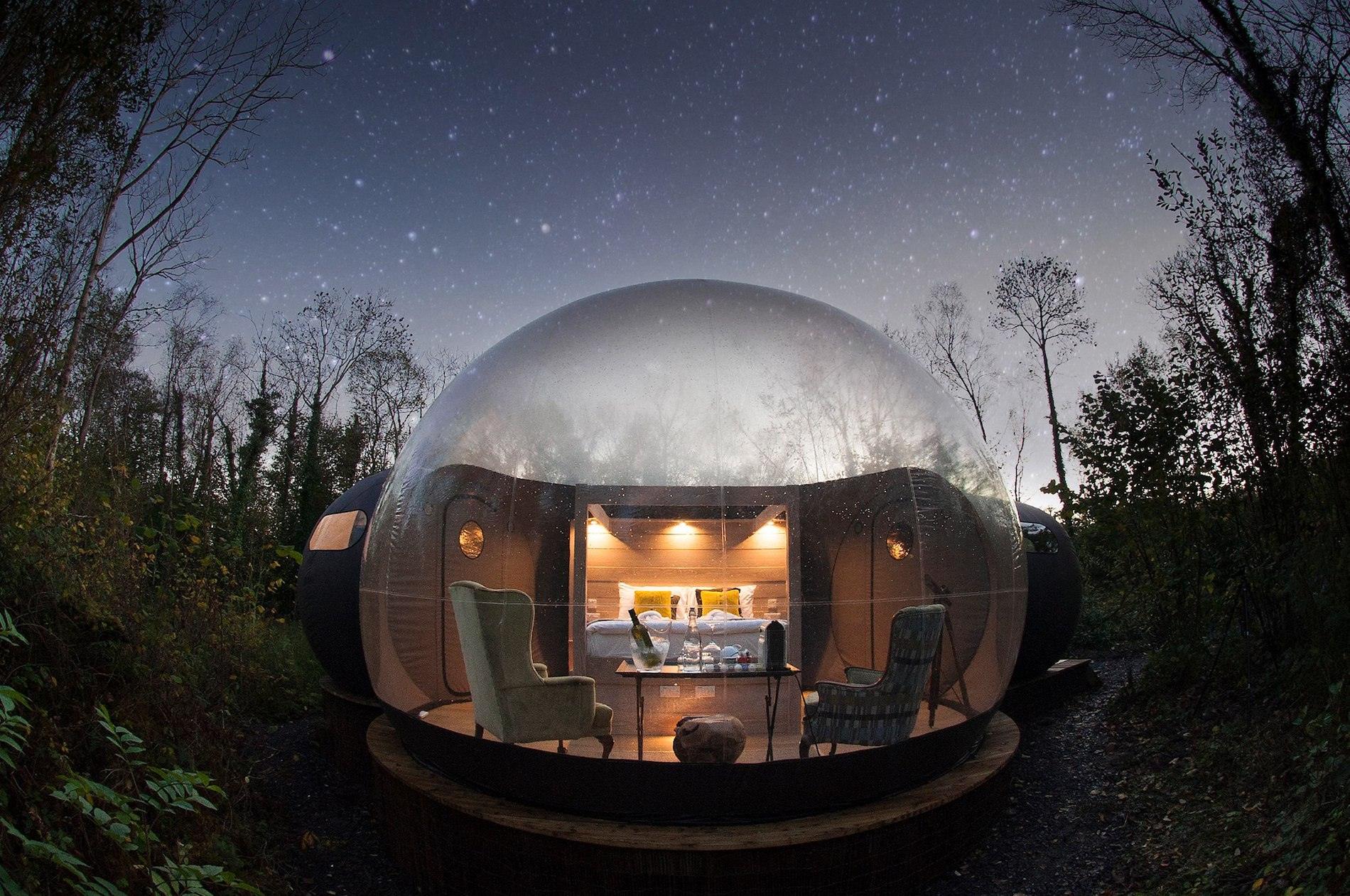 A lit dome glamping pod in the woods at Finn Lough, County Fermanagh, with stars visible through the trees.