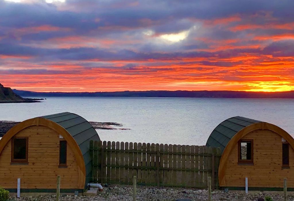 Wooden glamping pods on Rathlin Island, County Antrim, face a vibrant sunset over the sea.