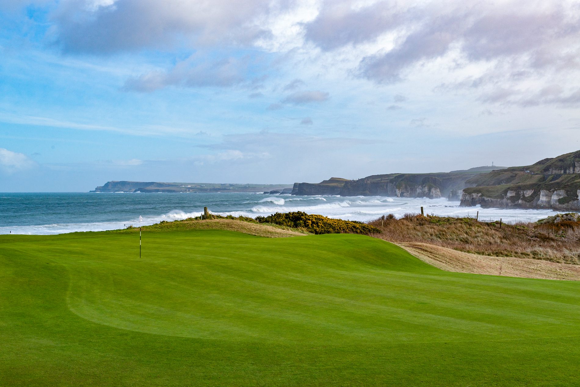 Coastal golf course green overlooking rugged cliffs and Atlantic waves in Northern Ireland.
