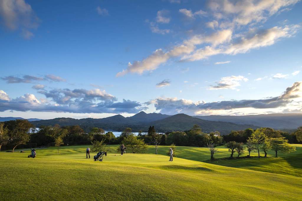 Golfers on the green at Glengarriff Golf Club overlook Bantry Bay with mountains rising in the background.