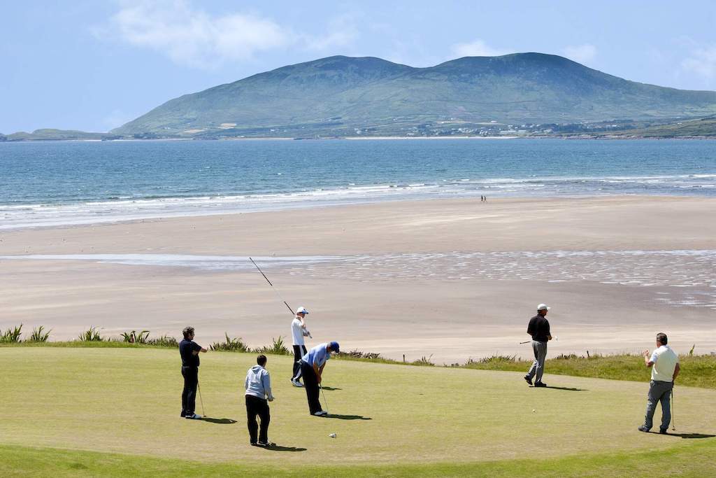 Golfers play by the shore at Waterville Golf Links with the Atlantic Ocean and mountains in the distance.