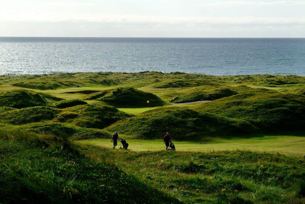 Golfers walk the rugged fairways of Strandhill Golf Club with the Atlantic Ocean stretching beyond the course.