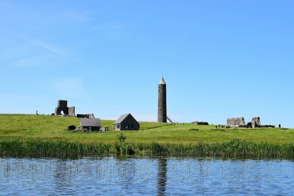 Devenish Island with a round tower and medieval ruins rising above green fields beside Lough Erne.