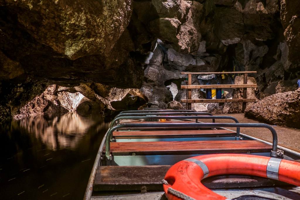 Wooden boat inside Marble Arch Caves floating on dark underground river below rock formations.