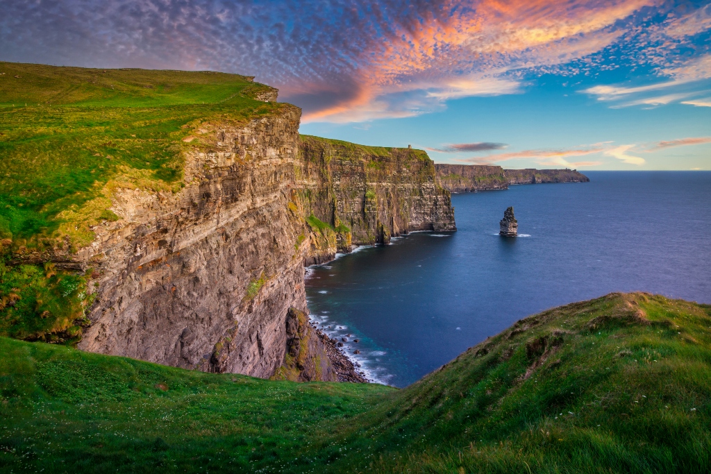 Cliffs of Moher stretching along the Atlantic coast at sunset, sheer rock faces meeting deep blue ocean waves.