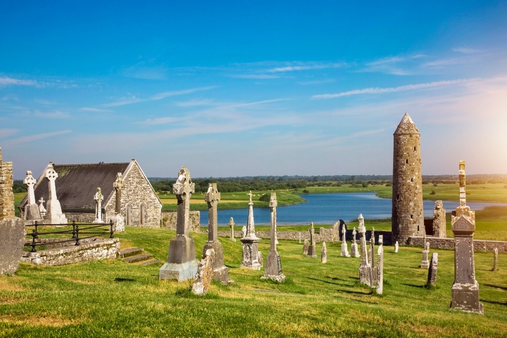 Clonmacnoise Monastic Site showing ancient round tower, Celtic crosses and stone church beside the River Shannon.