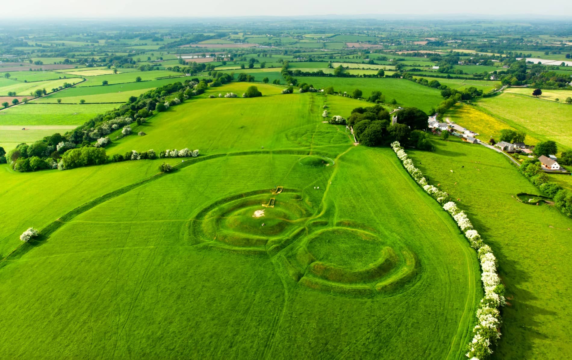 Aerial view of the Hill of Tara’s ancient earthworks surrounded by lush Meath countryside under a clear sky.