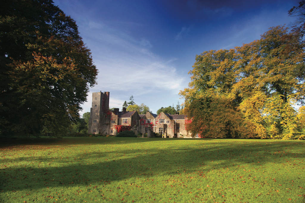 Autumn trees surround Belle Isle Castle manor with ivy-covered walls under a dramatic blue sky.