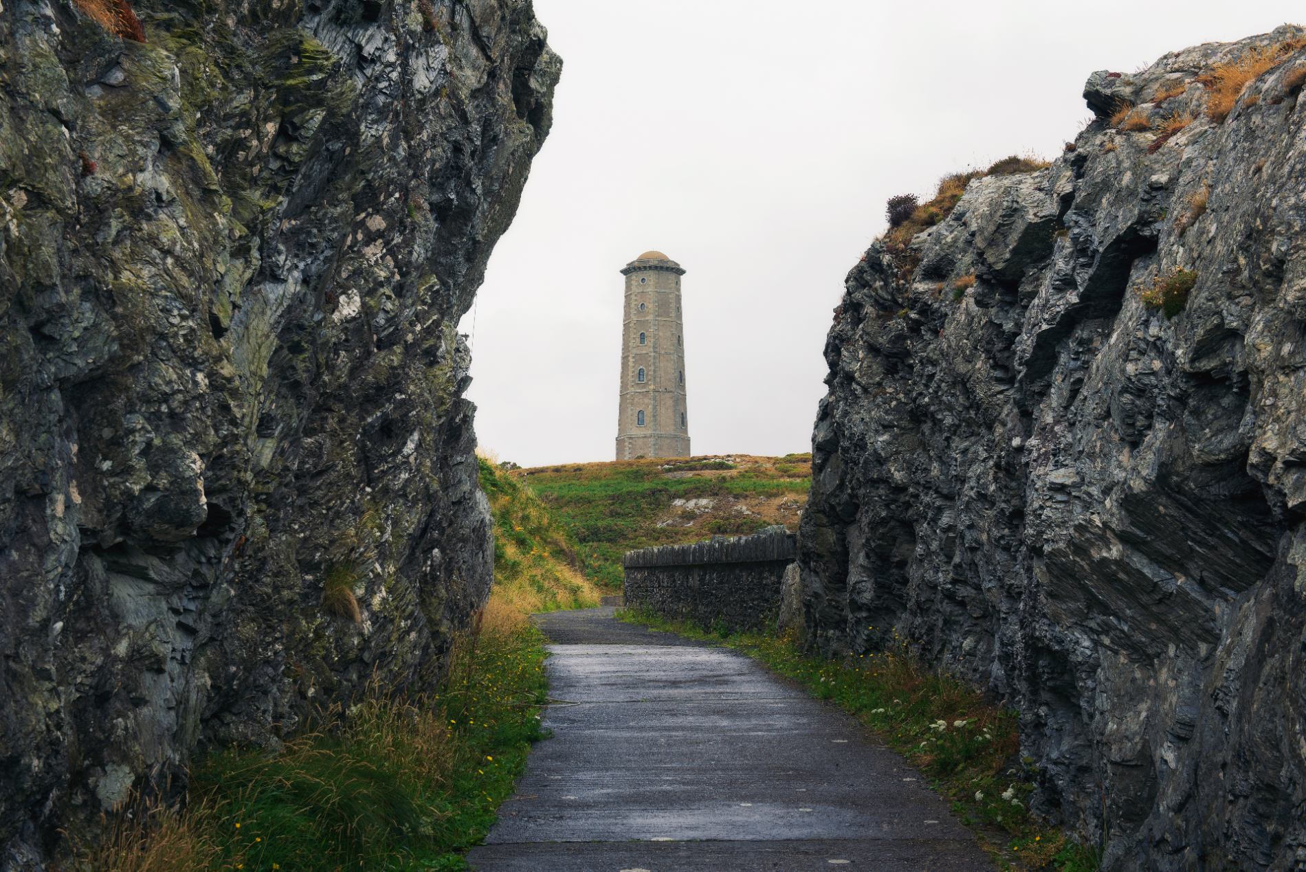 Tall stone tower framed by rugged sea cliffs along a walking trail near a historic coastal site in Ireland.