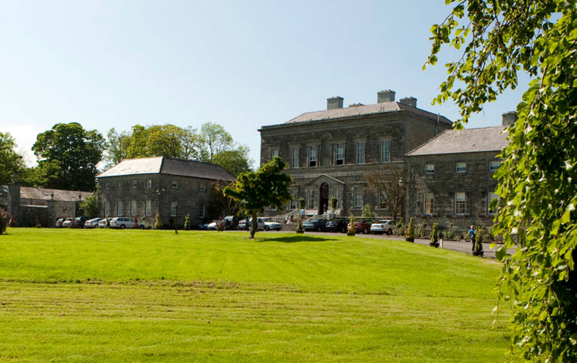 Georgian-style Bellinter House in County Meath, fronted by manicured lawns and parked cars under a clear sky.