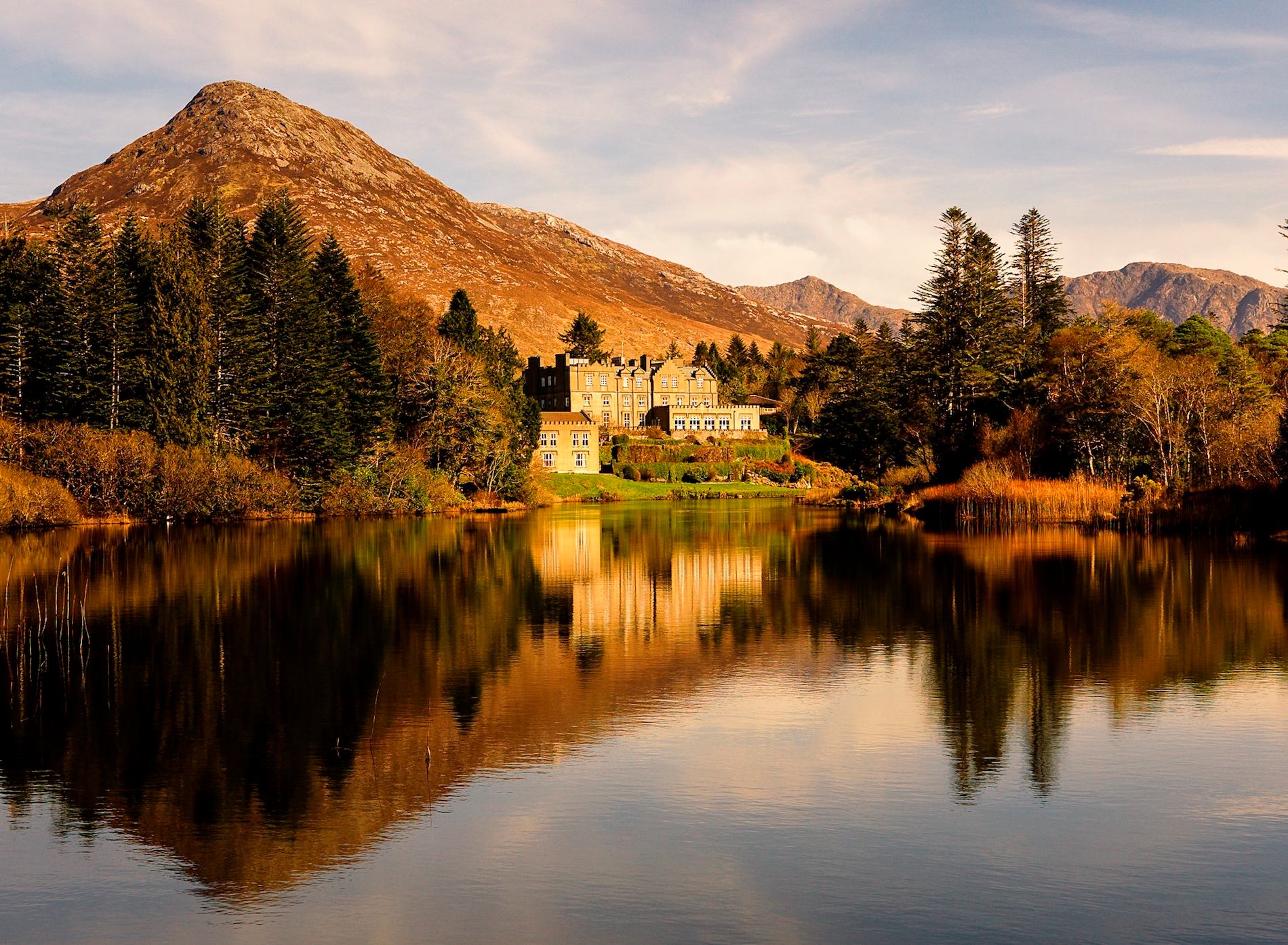 Grand lakeside hotel, Ballynahinch Castle, framed by autumn trees and mountains in the scenic Galway countryside.