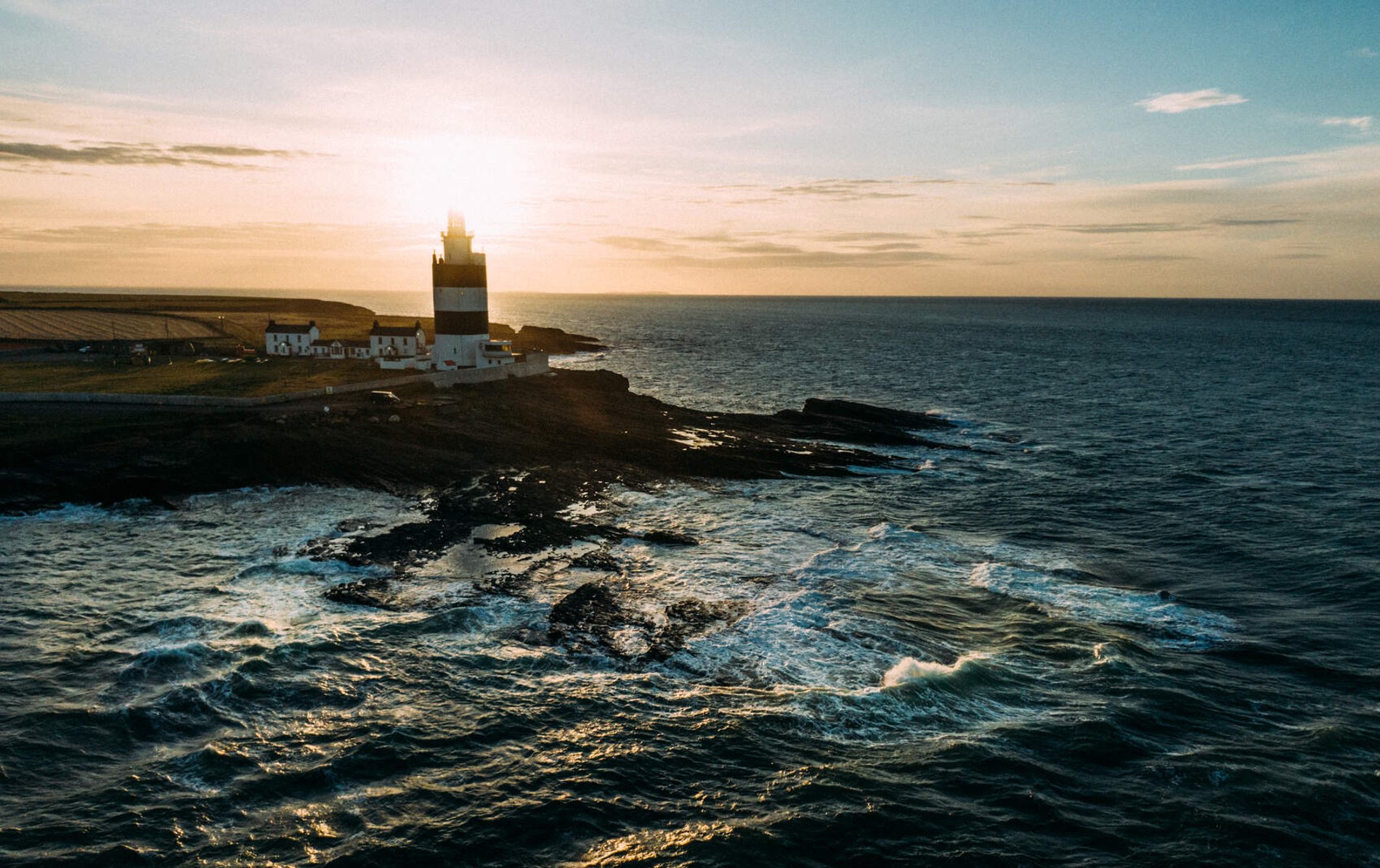 Lighthouse on Hook Head in County Wexford at sunset with the sun setting behind the tower.