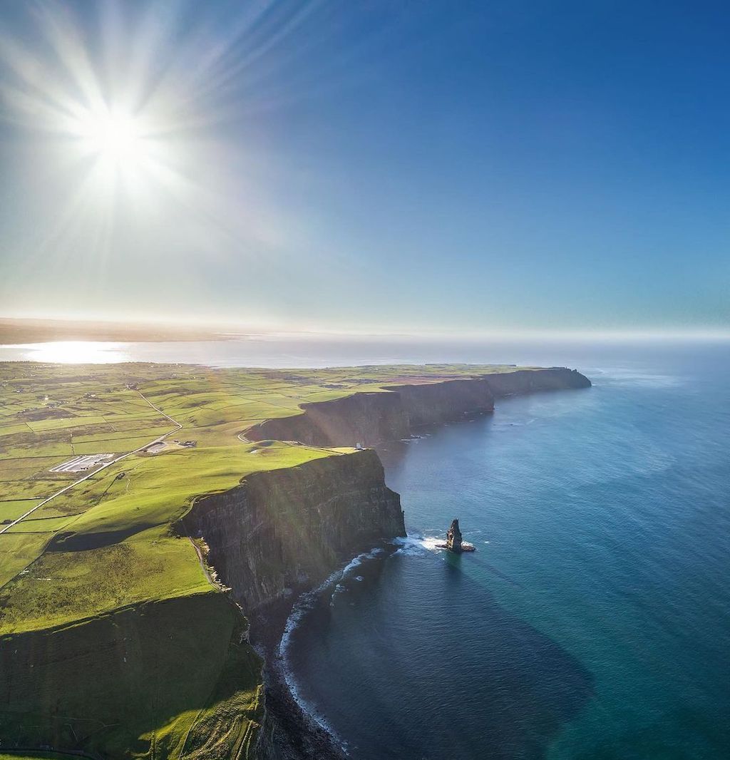 Aerial panorama of the Cliffs of Moher in County Clare, towering over the Atlantic Ocean beneath a bright sunlit sky.