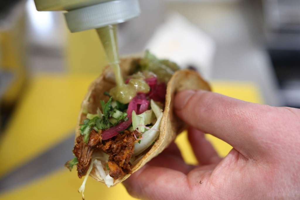 Close-up of a taco being filled with shredded meat, herbs, pickled onions, and green salsa at The Hungry Donkey in Kerry.