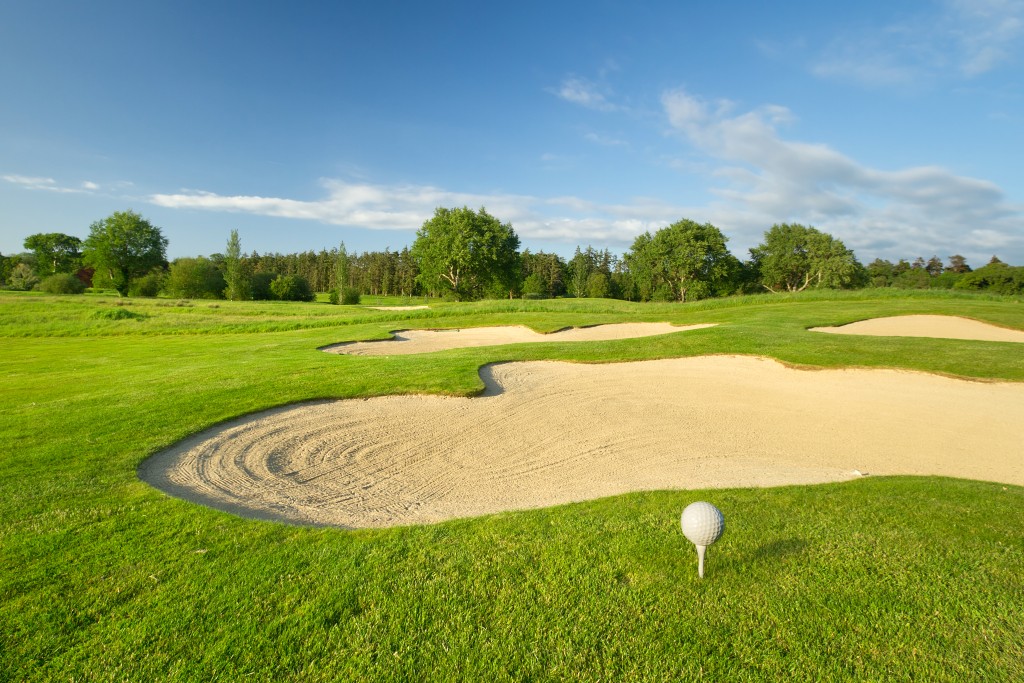 Golf ball on a tee beside a sand bunker on a bright green fairway, representing Paul McGinley.