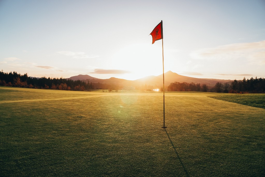 Flag on a golf green at sunset with mountains in the distance, representing Padraig Harrington.