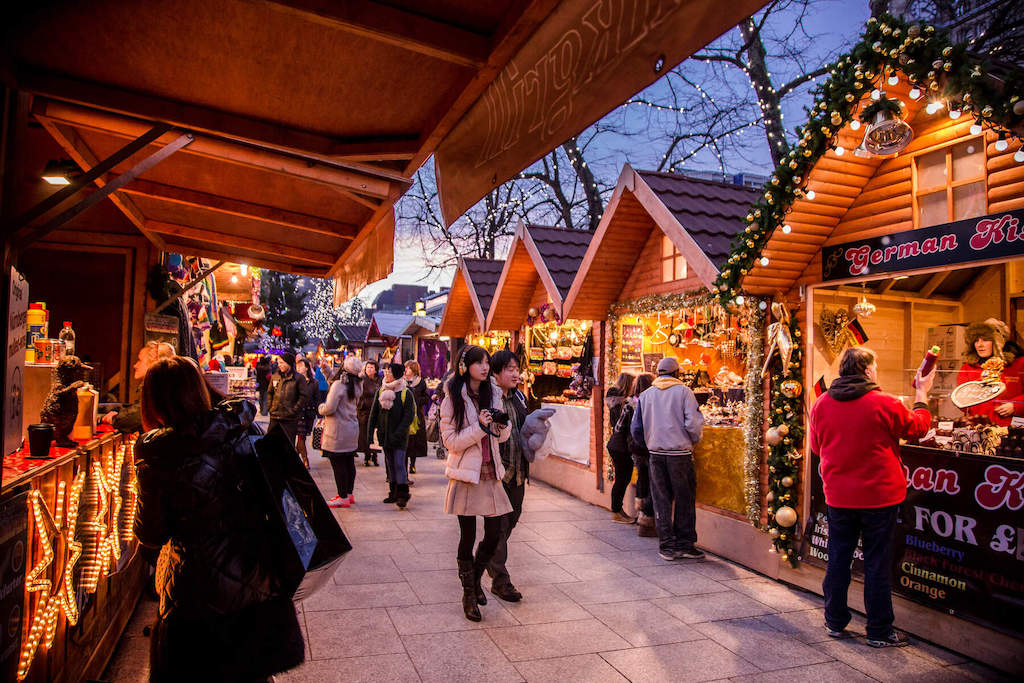 People browsing festive wooden stalls decorated with lights at Belfast Christmas Market.