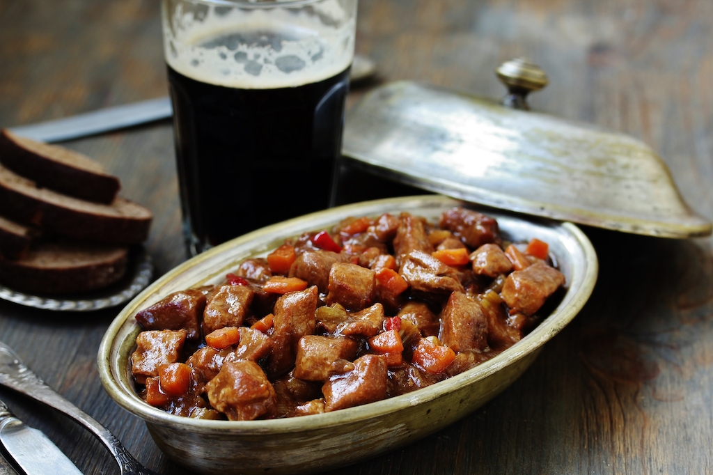 Traditional Irish beef stew with vegetables served beside dark stout and bread.