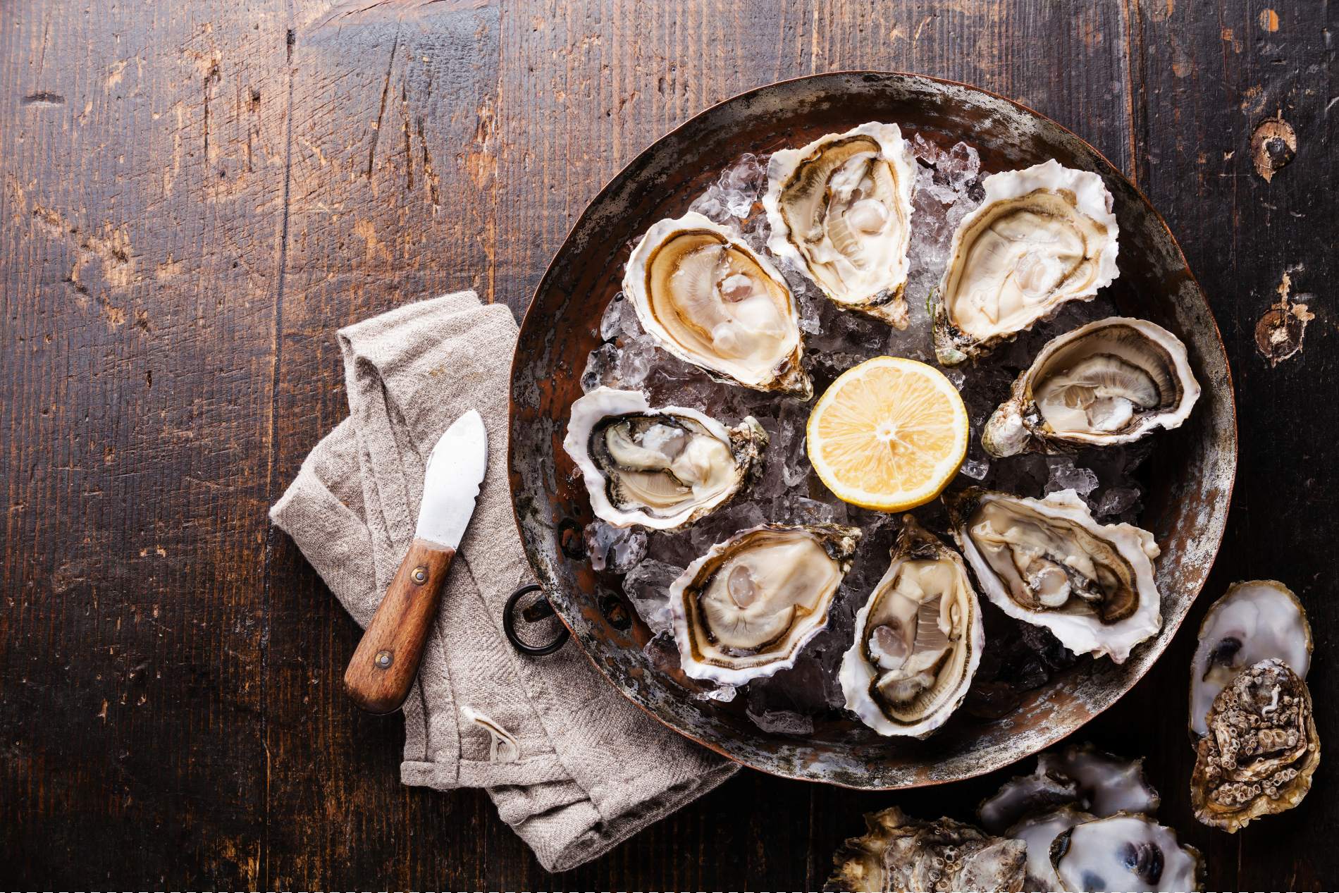 Plate of Irish oysters on ice with lemon, served with an oyster knife on a wooden table.