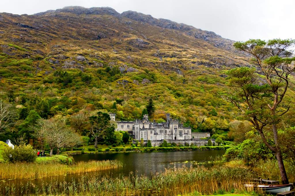 Gothic abbey beside a reflective lake, framed by lush forested mountain slopes.