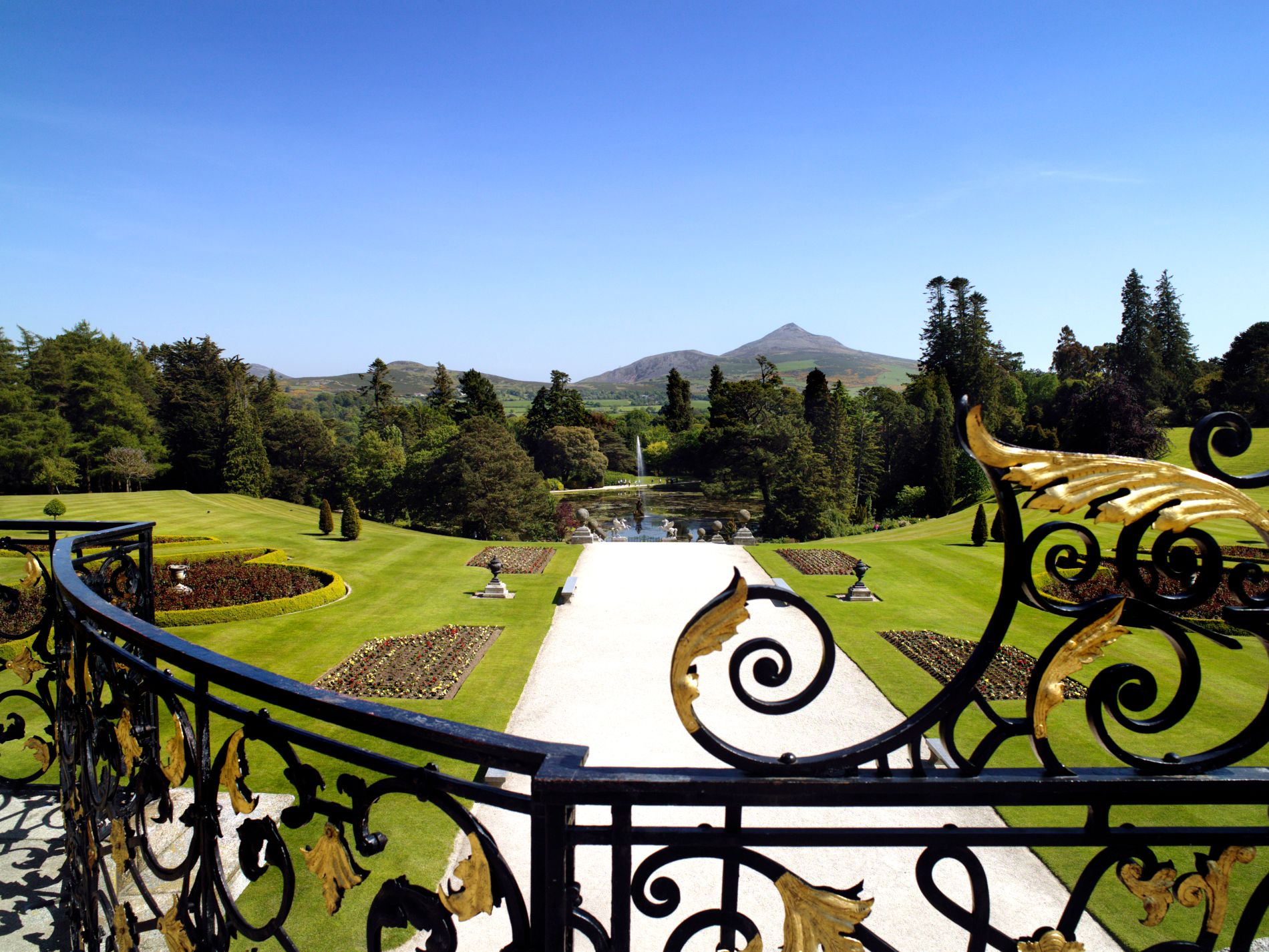 Ornamental gardens with mountain backdrop, fountains, and manicured lawns.