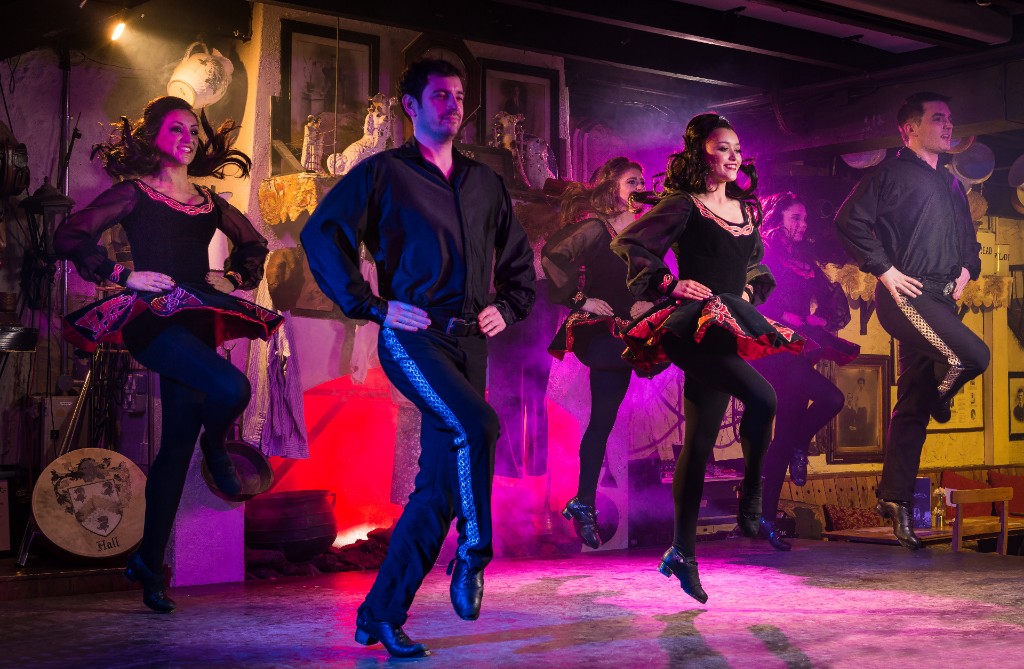 Irish dance troupe in black and red costumes perform on stage with purple lighting at Johnnie Fox's pub in County Dublin.