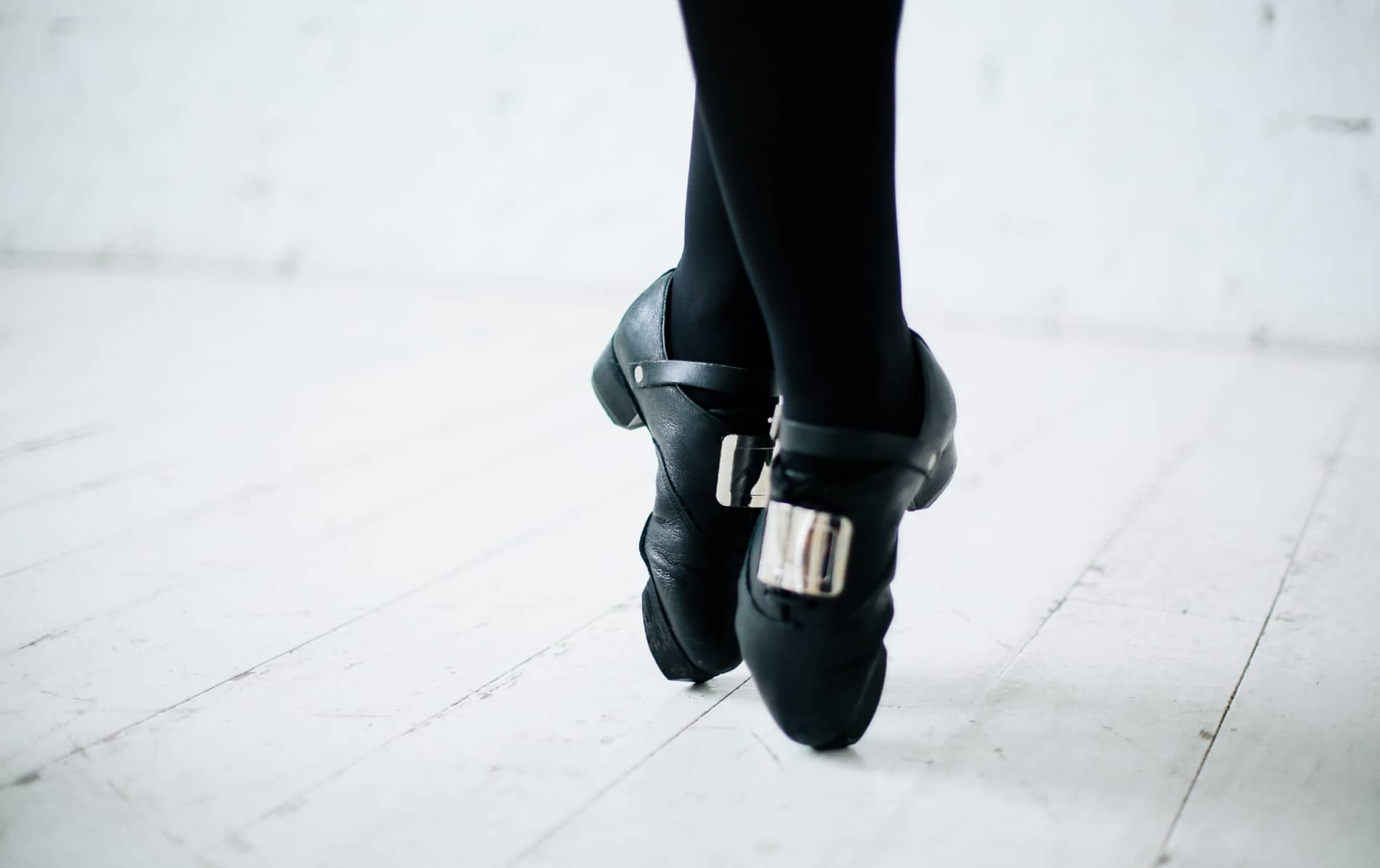 Close-up of Irish dancing shoes with metal taps worn by a dancer on a wooden floor.