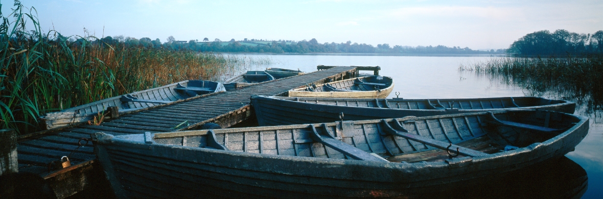 Row of wooden boats moored to a narrow jetty on the still waters of Lough Erne, County Fermanagh.