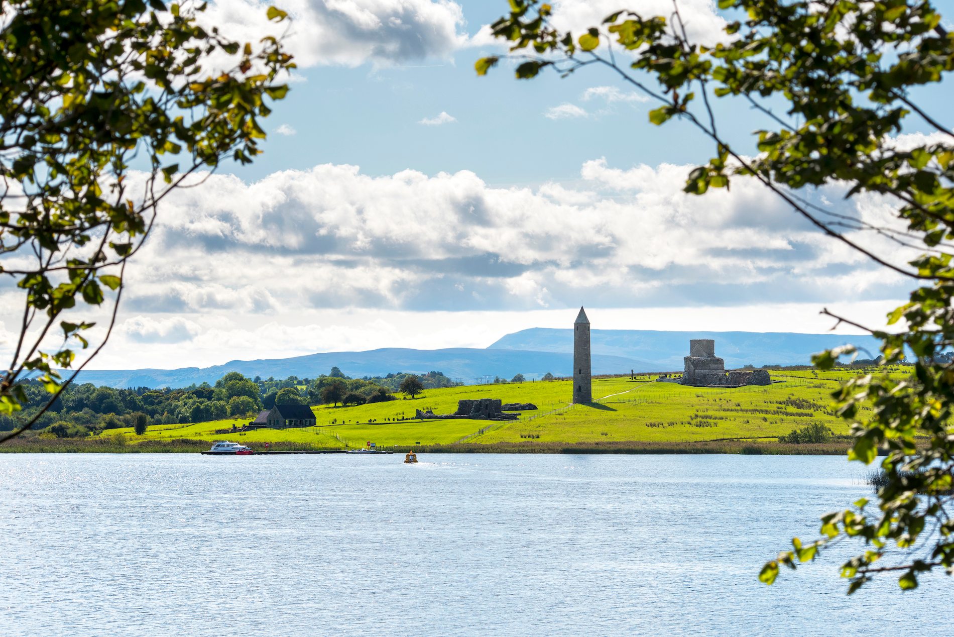 Panoramic view of Devenish Island on Lough Erne, County Fermanagh, with a round tower and church ruins framed by trees.