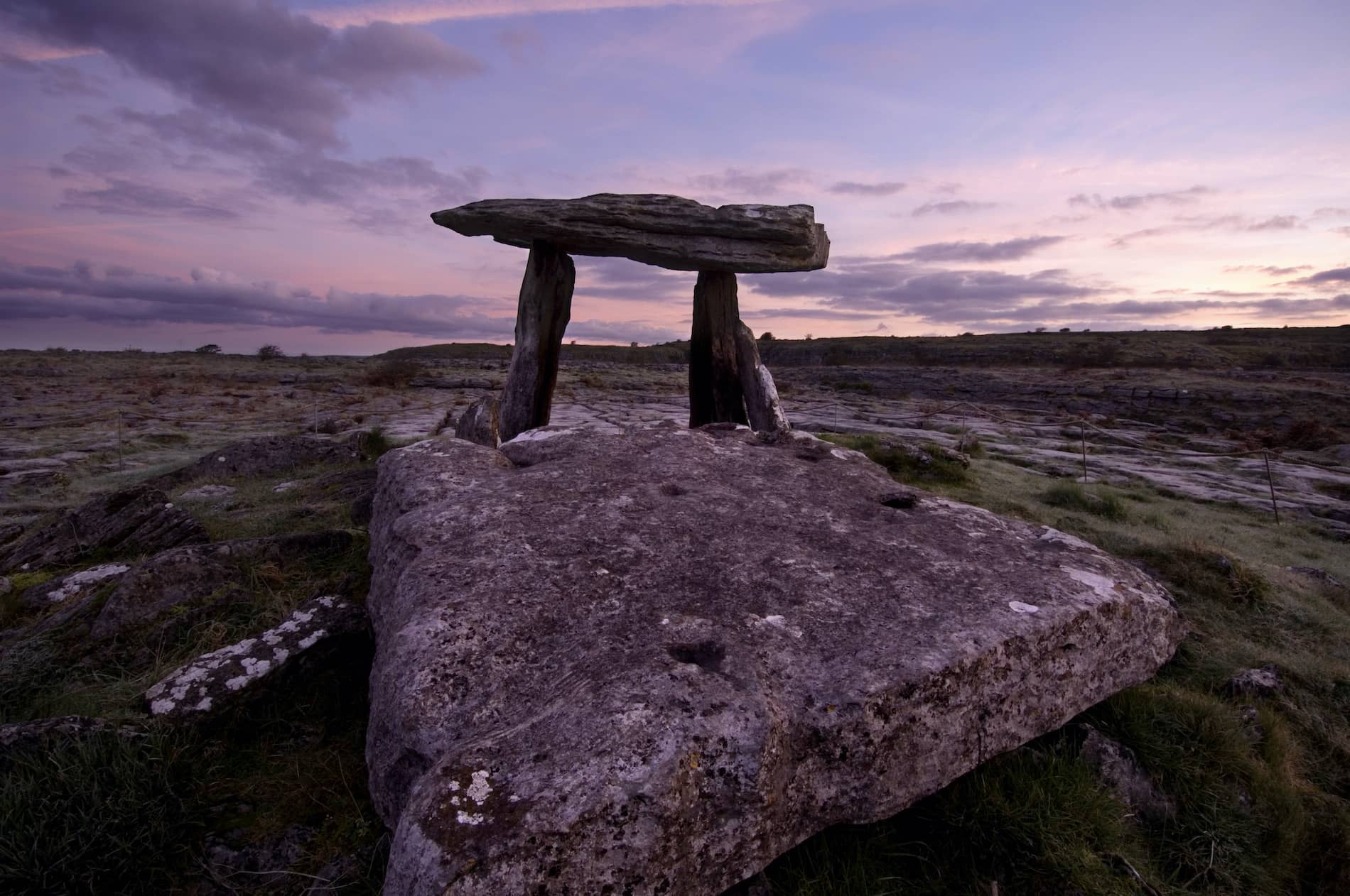 Karst limestone slabs of Poulnabrone Dolmen in the Burren, County Clare, at dusk with a purple sky overhead.