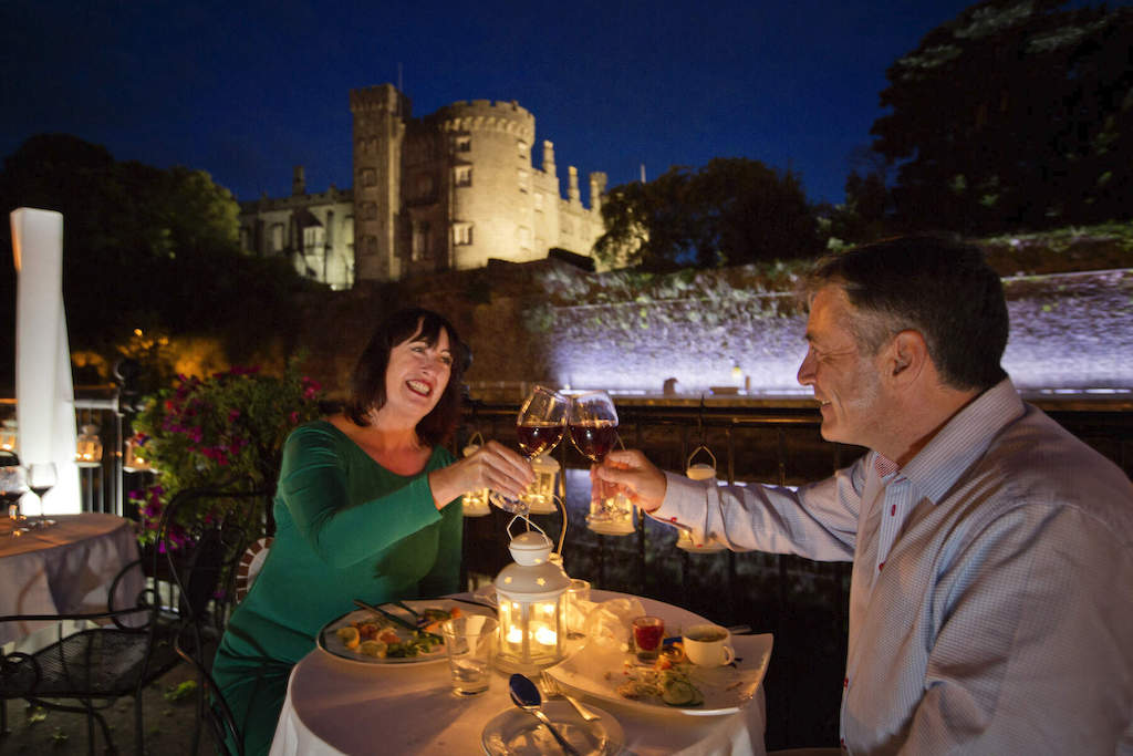 Couple enjoying candlelit dinner with Kilkenny Castle illuminated in the background.