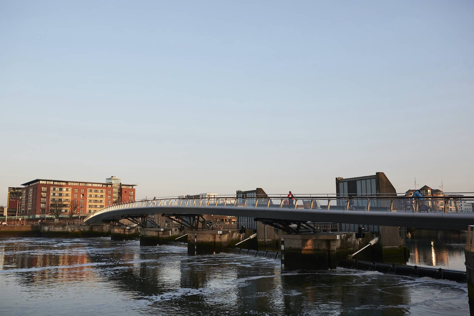 Lagan Bridge in Belfast spans the river, reflecting city buildings in the water at golden hour.