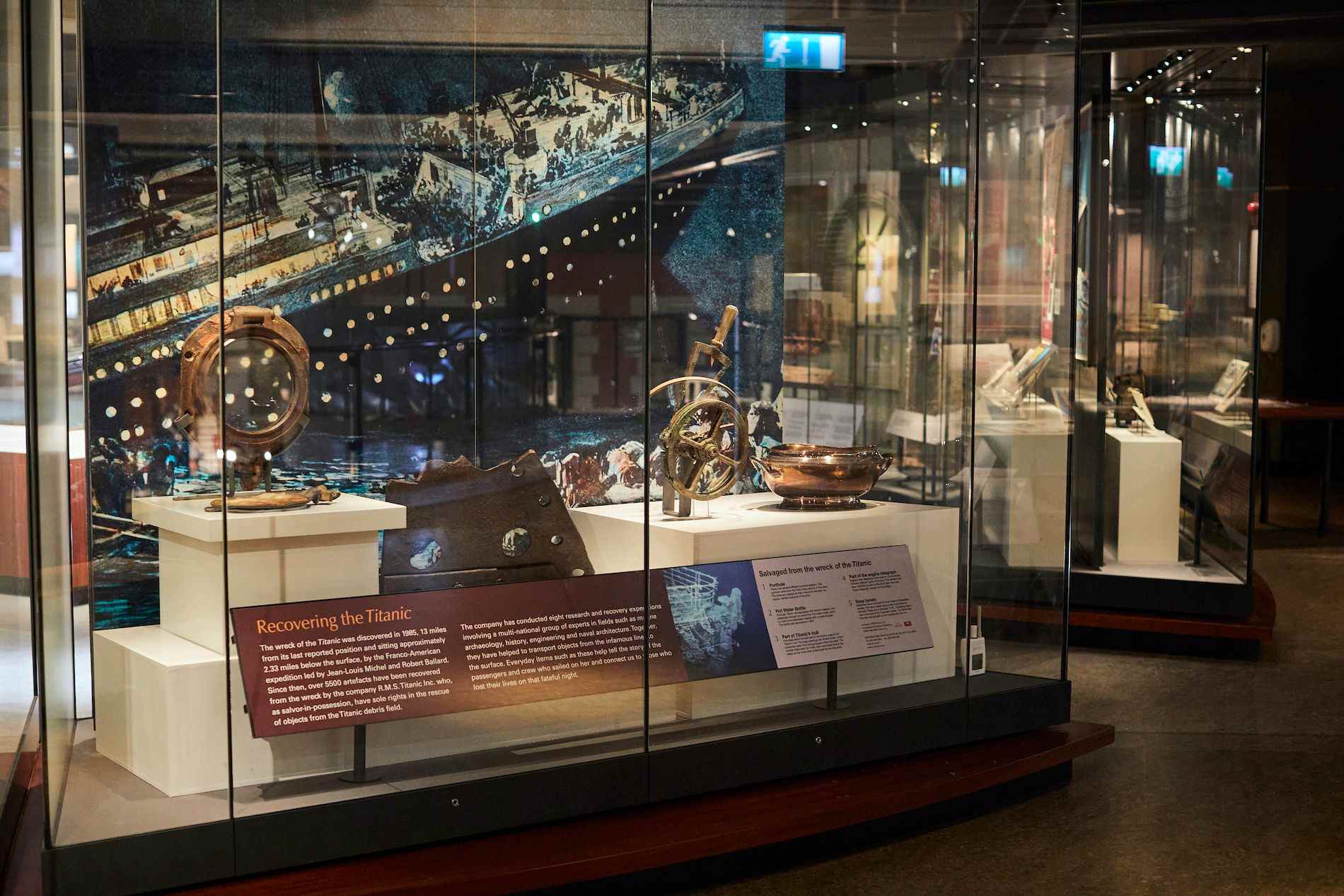 Display of recovered Titanic artefacts, including a porthole and navigation instruments, in a museum case.
