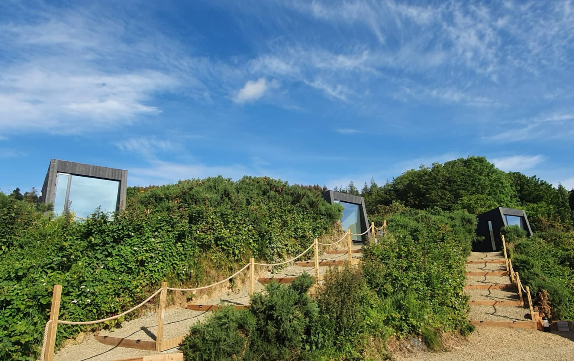 Tara Hill Estate glamping cabins with mirrored glass set into green shrubland under a bright blue sky in Wexford.