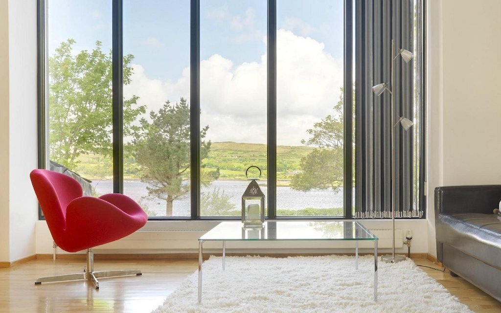 Contemporary Blairscove House with red chair and lake views framed by floor-to-ceiling glass windows in County Cork.