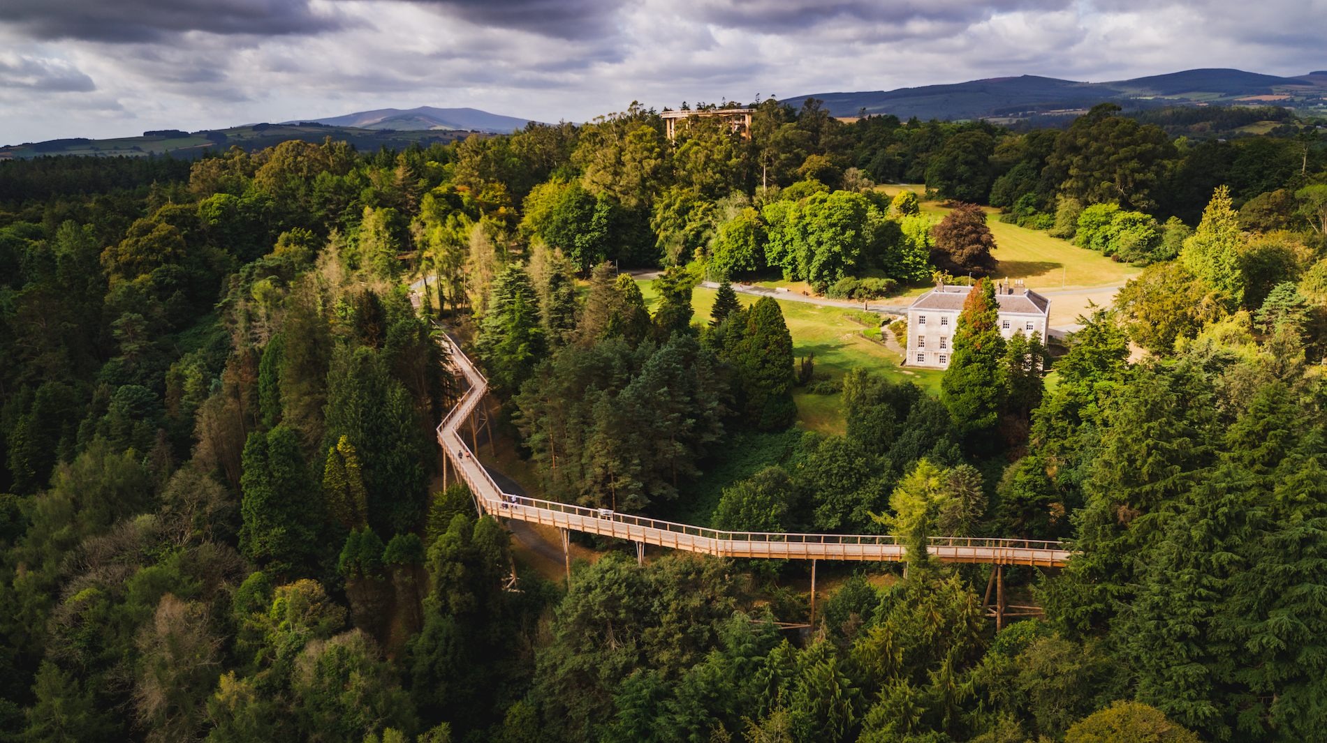 Treetop walkway winds through lush forest beside a historic house at Avondale Forest Park, County Wicklow.