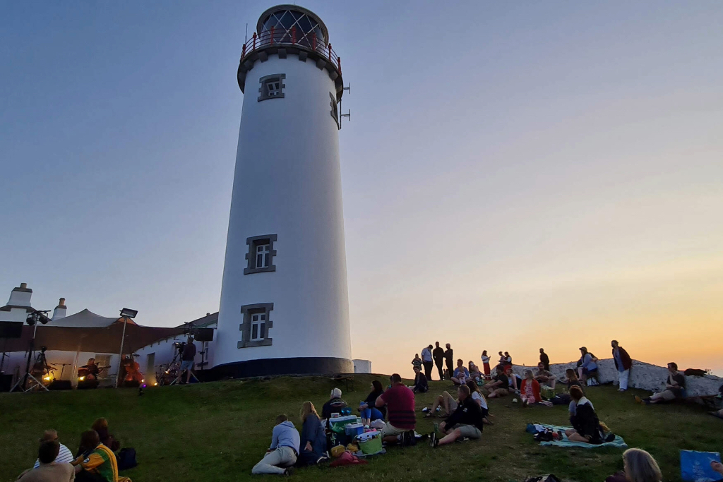People relax on the grass beside Fanad Lighthouse in Donegal during Earagail Arts Festival at sunset.