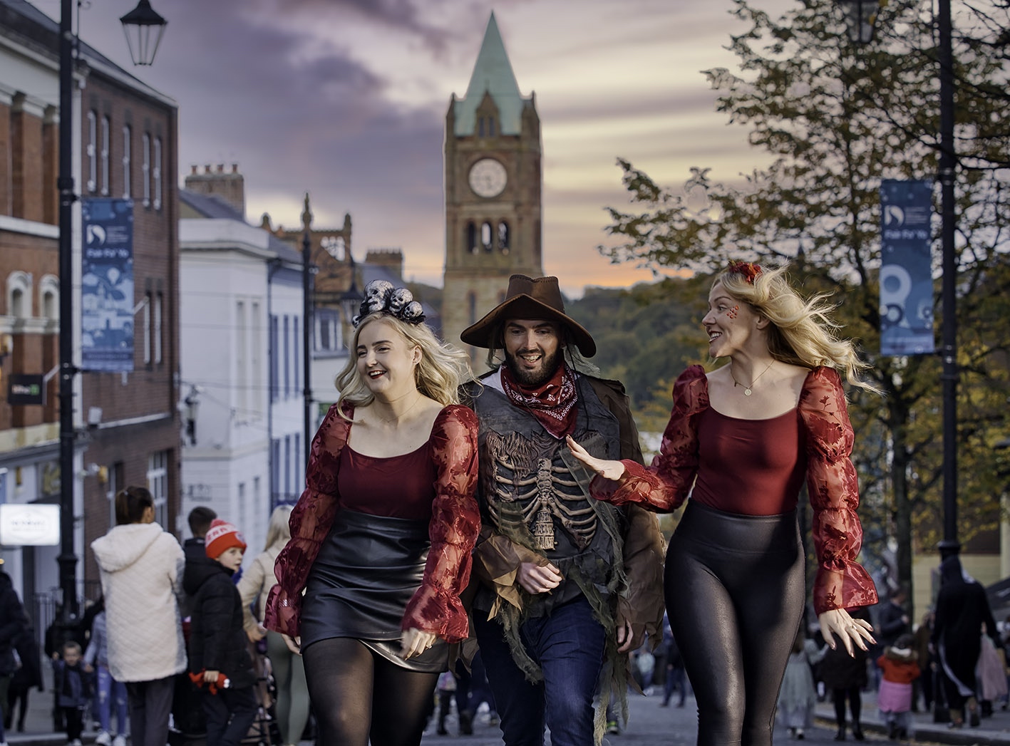 People in costume walk through the streets of Derry during Halloween celebrations, with the Guildhall clock behind.