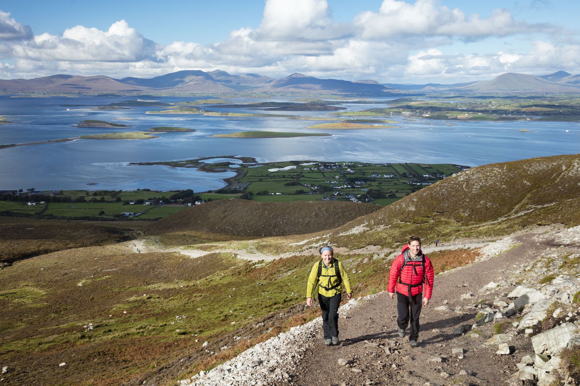 A couple hike a trail on Croagh Patrick in Mayo, with Clew Bay and its many islands stretching out behind them.
