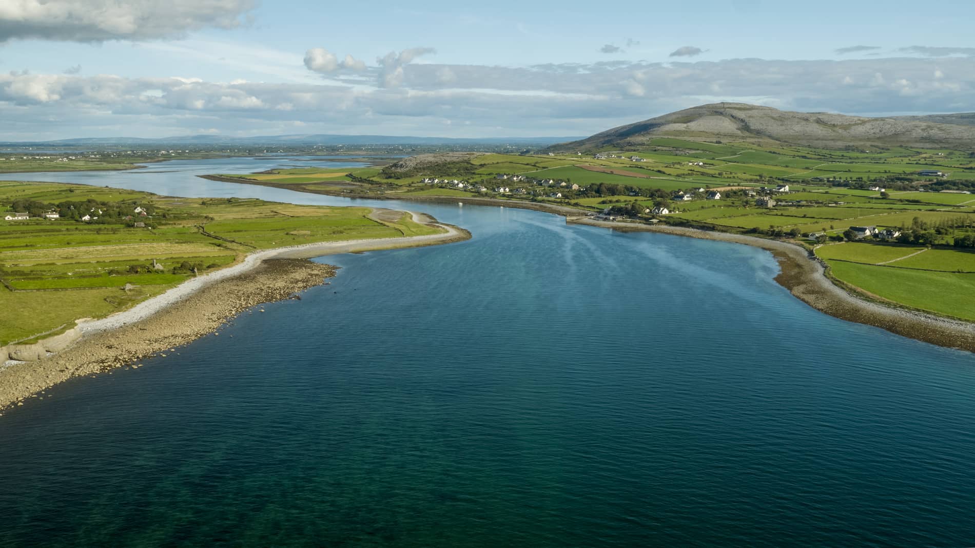 A peaceful inlet at Flaggy Shore, Clare, with blue water winding through green fields and scattered houses.