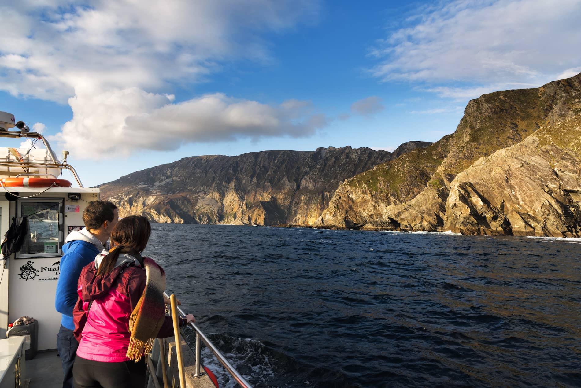 Two people on a boat admire the sea cliffs of Slieve League, rising steeply from the Atlantic in Donegal.