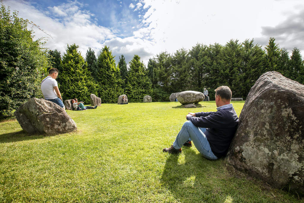 Visitors relaxing beside boulders in the peaceful green setting of the stone circle in Kenmare, Kerry.