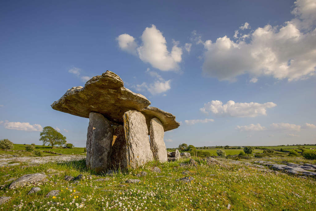 Poulnabrone Dolmen on a wildflower-covered limestone plain in the Burren, Clare, beneath a blue sky.