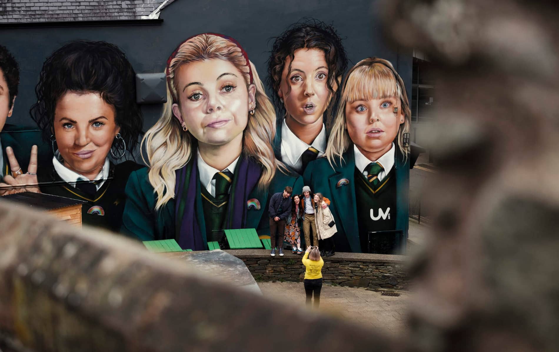 Tourists pose in front of the Derry Girls mural, showing five schoolgirls in uniform on Orchard Street.