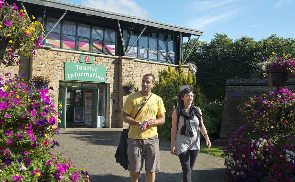 Couple walks past colourful flowers outside Derry’s stone-clad Visitor Information Centre.