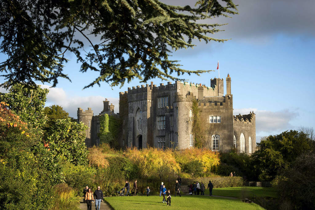 Visitors strolling the gardens outside Birr Castle in County Offaly, framed by autumn trees and dramatic Gothic turrets.
